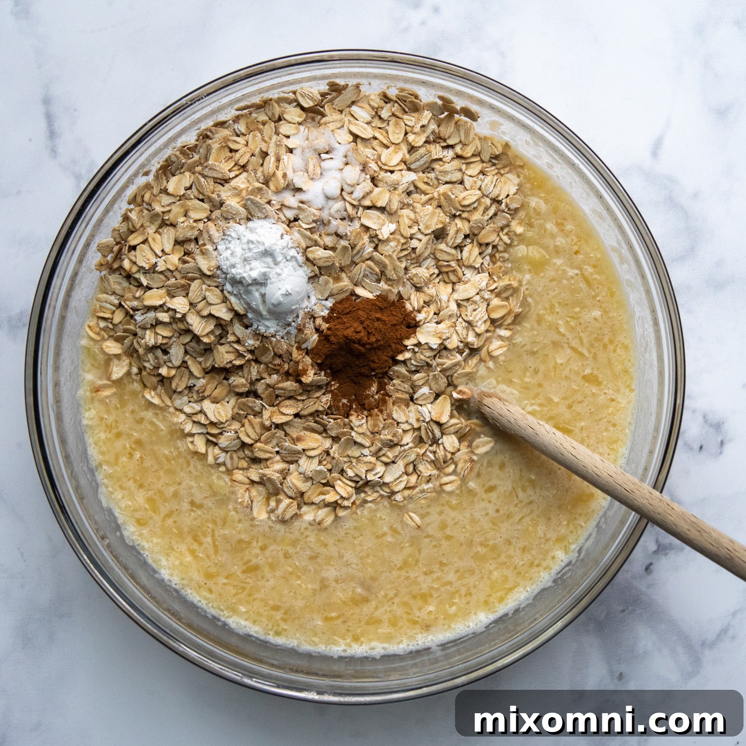 Gluten-free oats and dry spices being gently stirred into the banana and liquid mixture.
