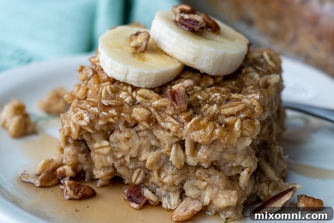 A close-up shot of a serving of banana baked oatmeal, generously topped with fresh banana slices and chopped nuts.
