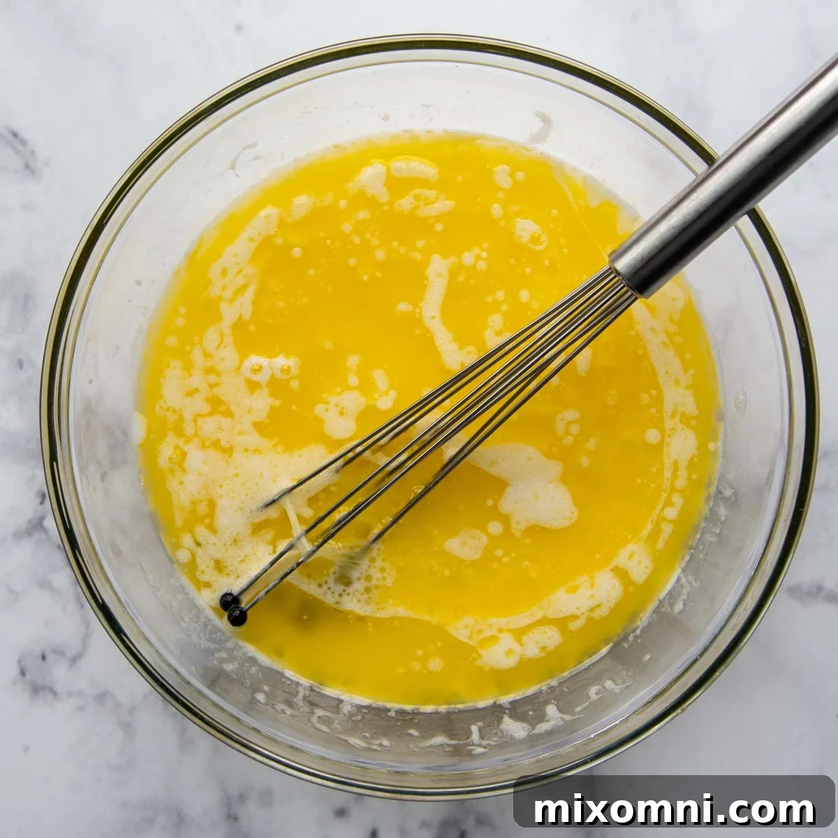 Wet ingredients (melted butter, milk, egg whites, vanilla) being whisked together in a glass bowl.