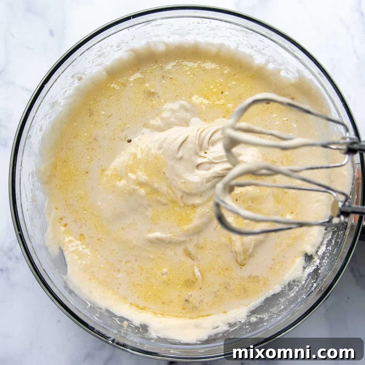 Gluten-free cake batter being mixed in a stand mixer, showing its pale and fluffy texture.
