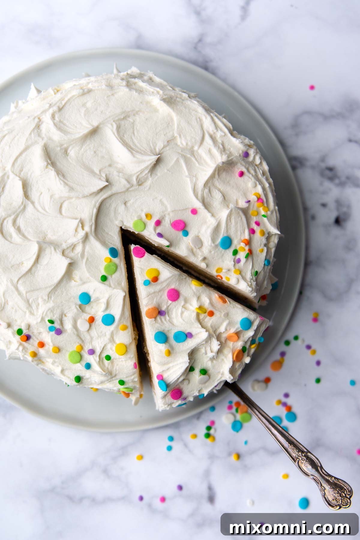 Overhead shot of a perfect slice of white cake being carefully lifted from a whole gluten-free cake.