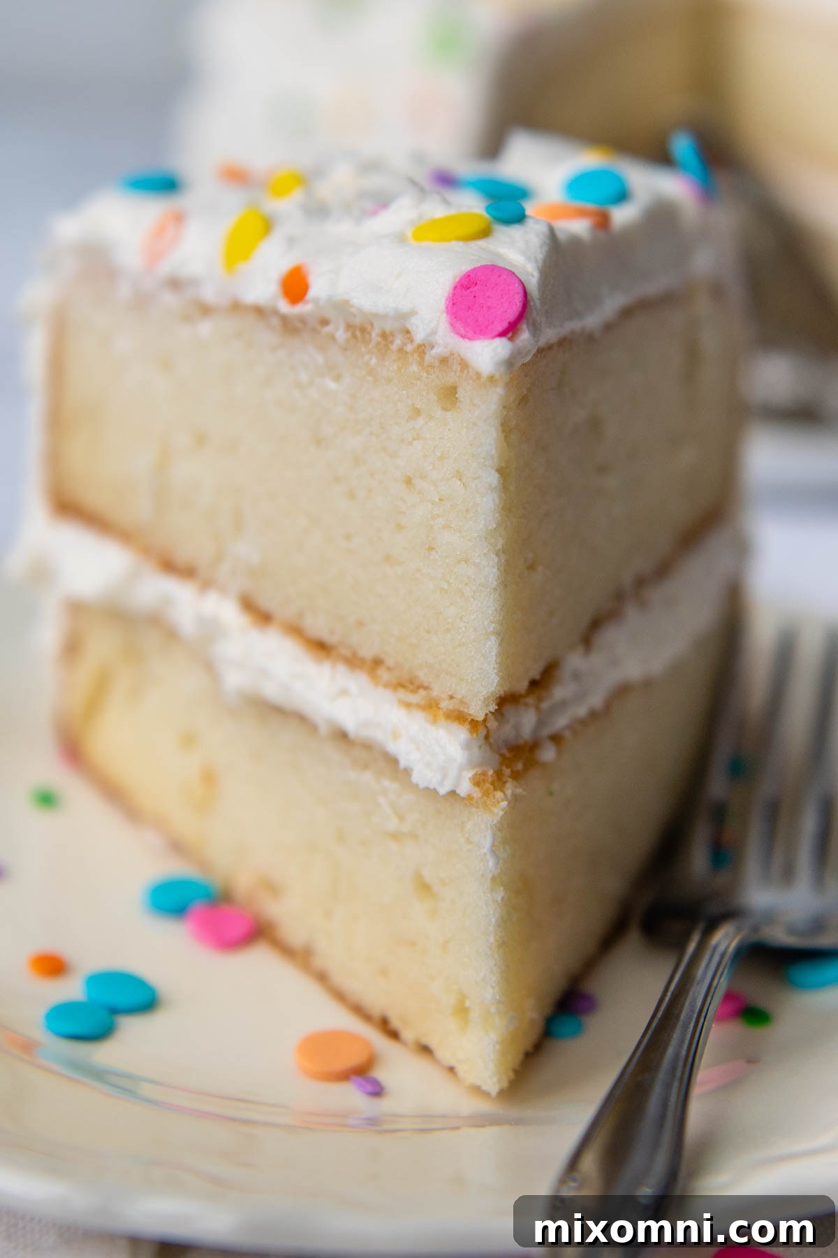 A perfectly cut slice of gluten-free white cake, showcasing its fluffy and moist interior, with frosting visible.
