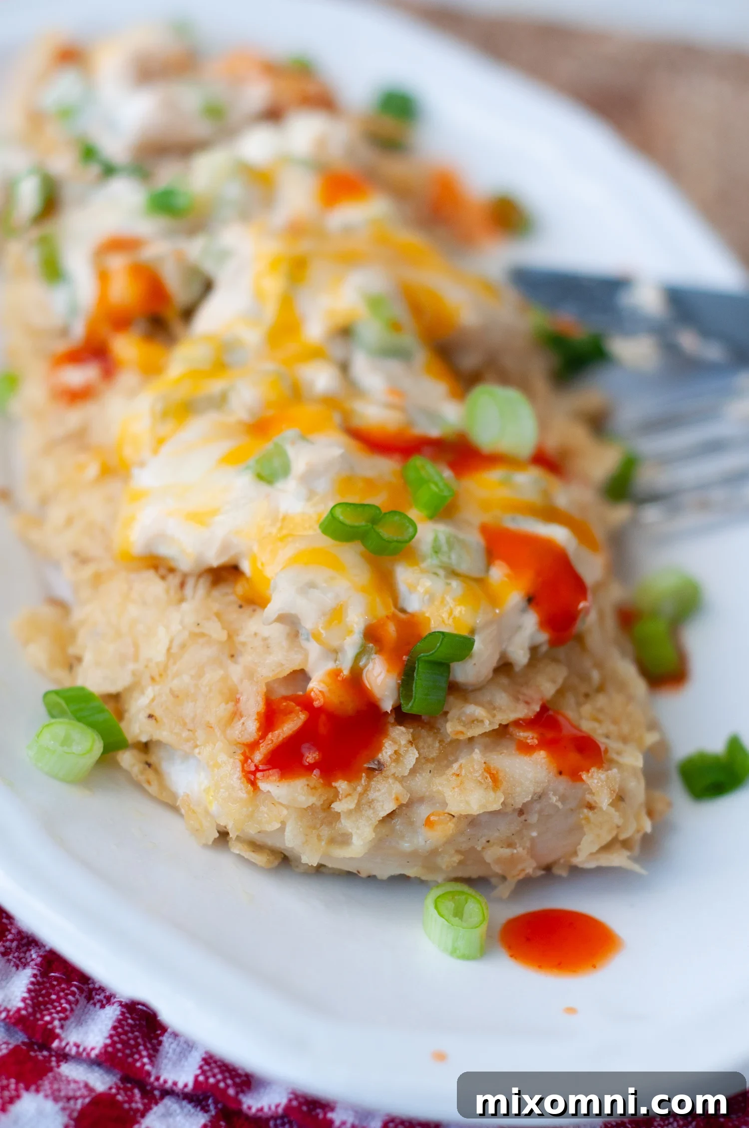 A serving of crispy, baked Buffalo Chicken with crushed tortilla chips and hot sauce drizzled over top, ready to enjoy.