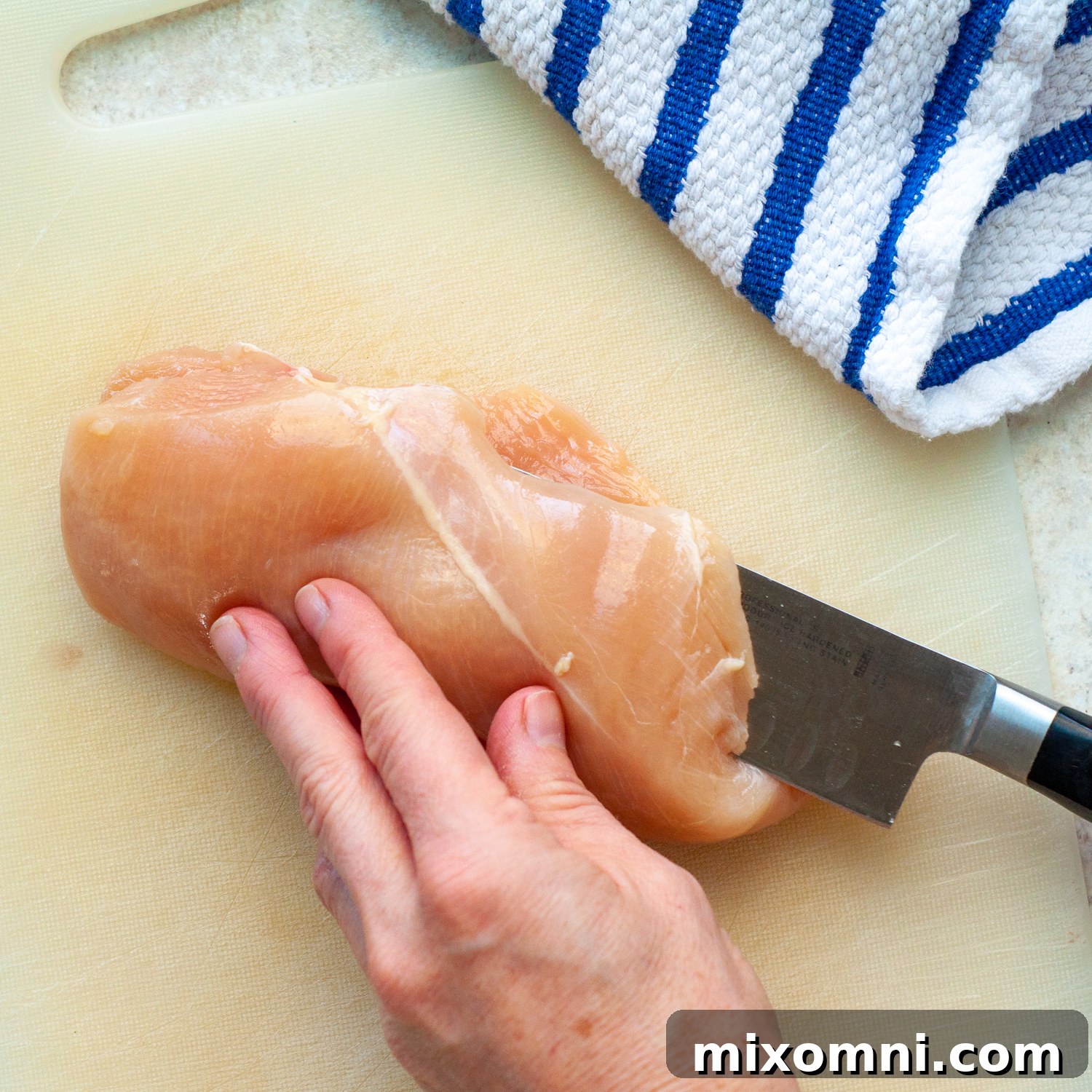 A knife carefully slicing a chicken breast horizontally to create a thinner cutlet.