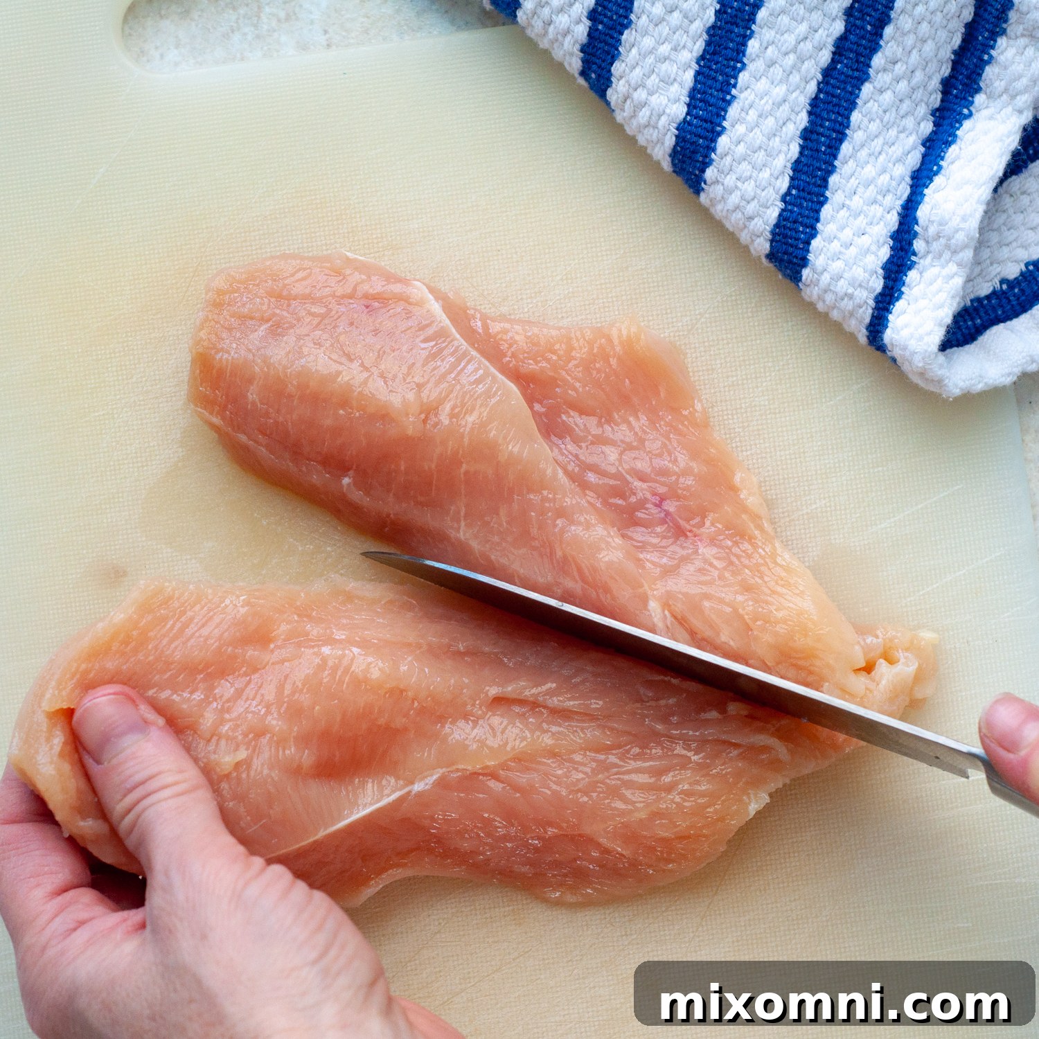 The butterflied chicken breast being further cut in half to create two even thinner cutlets.