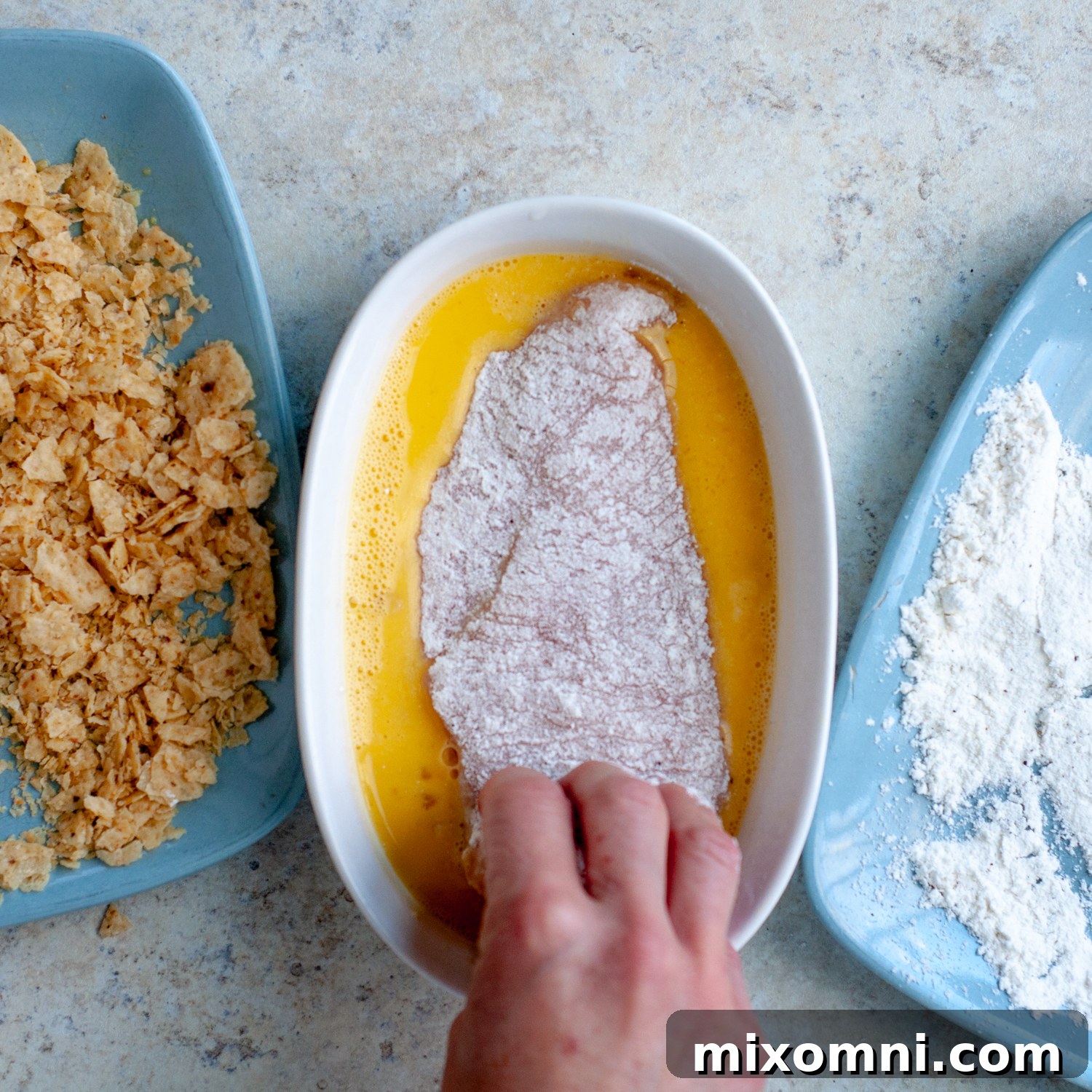 A chicken cutlet being coated evenly in seasoned flour as part of the dredging process.