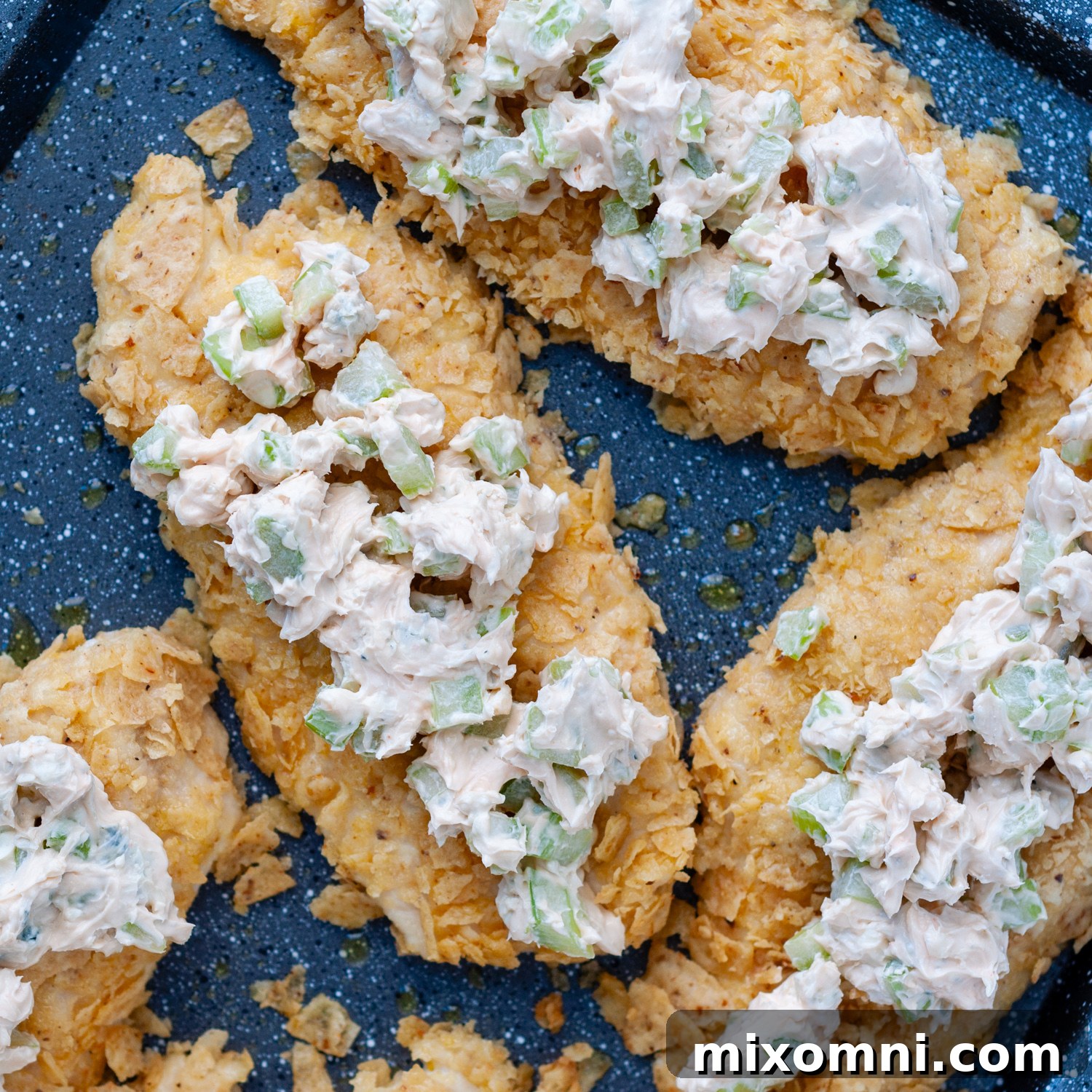 Cream cheese buffalo topping being spread over the baked, tortilla-crusted chicken.