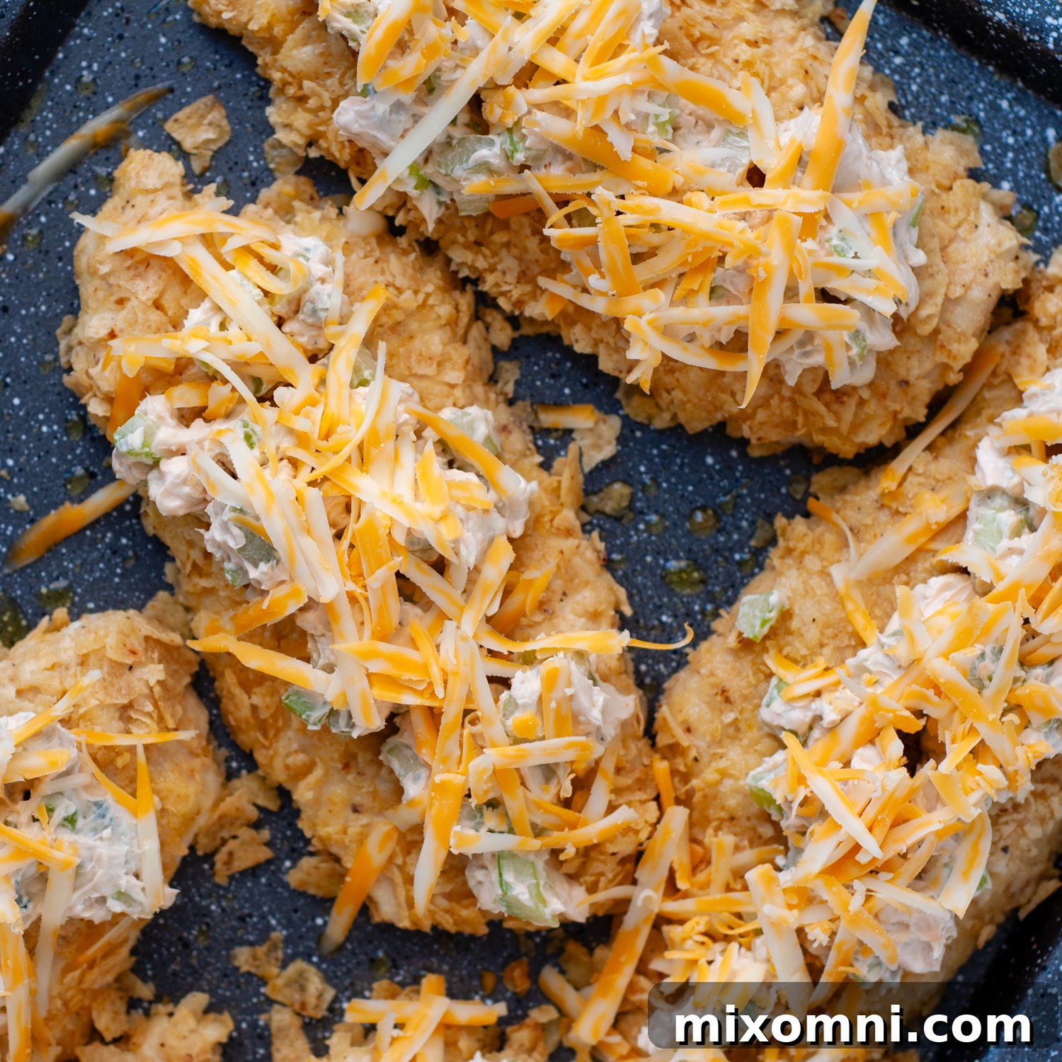 Shredded cheese generously sprinkled on top of the buffalo-topped chicken, ready for broiling.