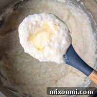 A scoop of grits with melted butter on top being held up from an Instant Pot.