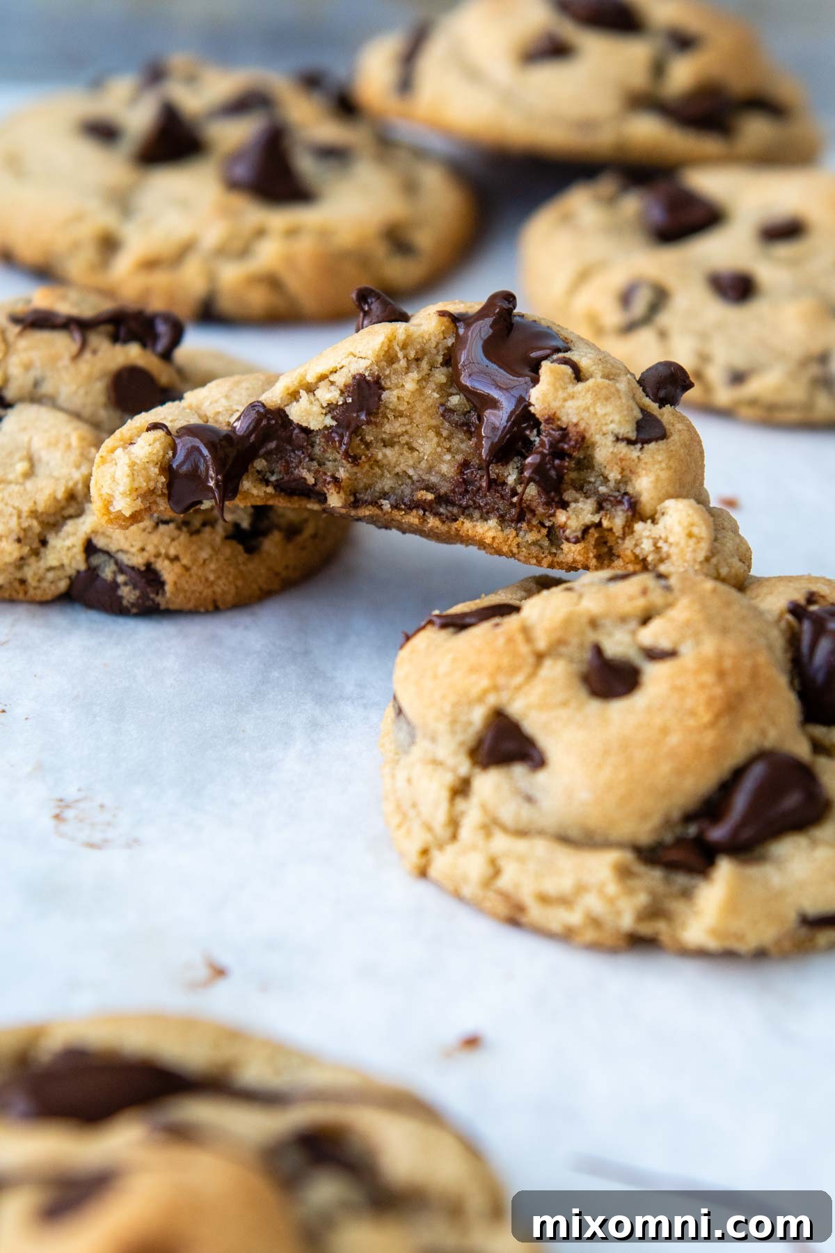 A perfectly baked almond flour chocolate chip cookie, bitten to reveal its soft, gooey interior, resting on two other cookies.