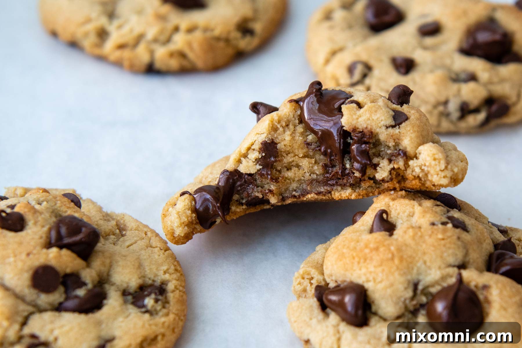 A close-up of a bitten almond flour cookie, revealing melted chocolate and a gooey texture, with mini and regular chocolate chips visible.
