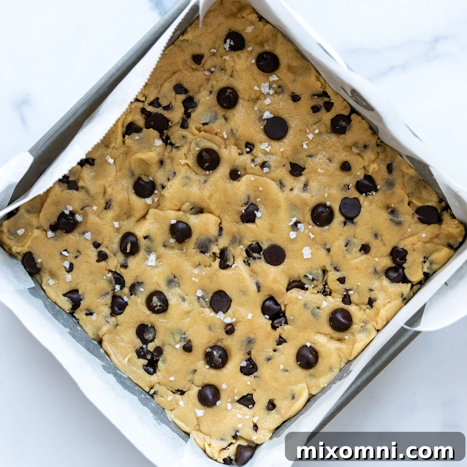 Gluten-free cookie dough pressed evenly into a metal baking pan, ready for chilling.