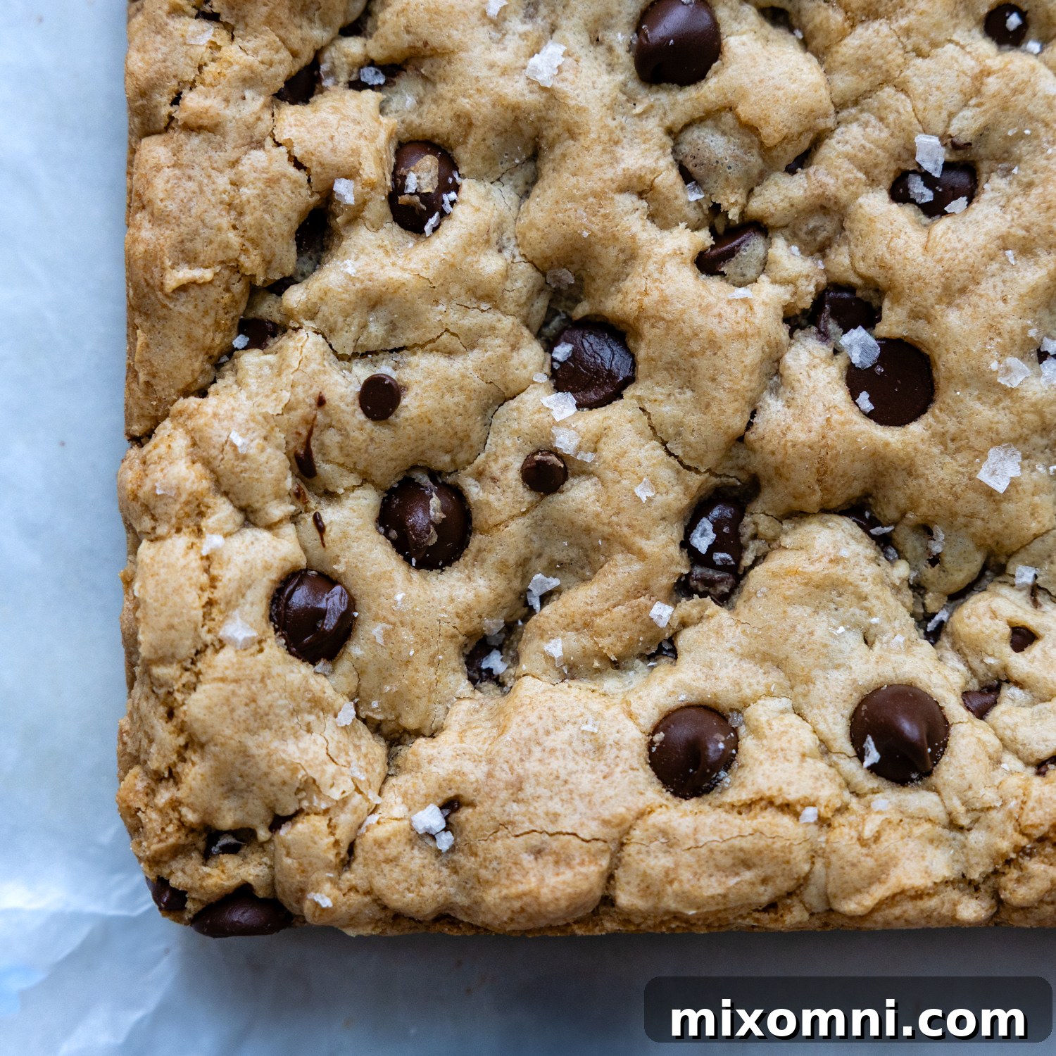 Baked gluten-free chocolate chip cookie bars, topped with flaky sea salt, on a white marble surface, ready to cool.