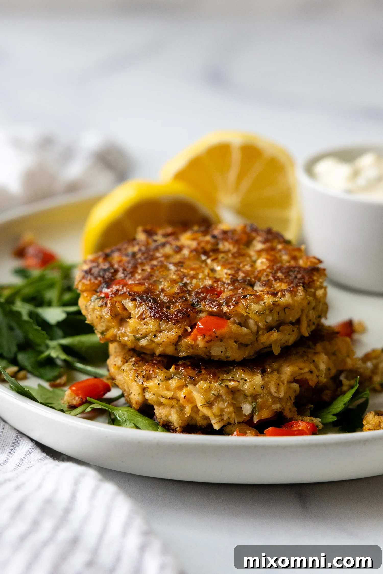 Gluten free salmon patties stacked on top of one another on a white plate, garnished with fresh dill and lemon wedges.