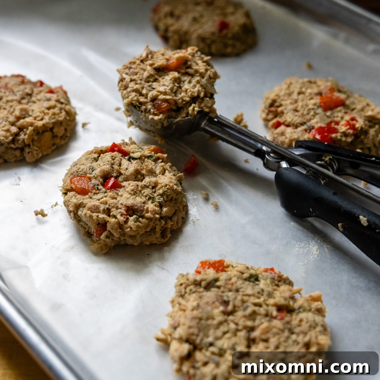 Scoop placing uncooked salmon patties on parchment paper.