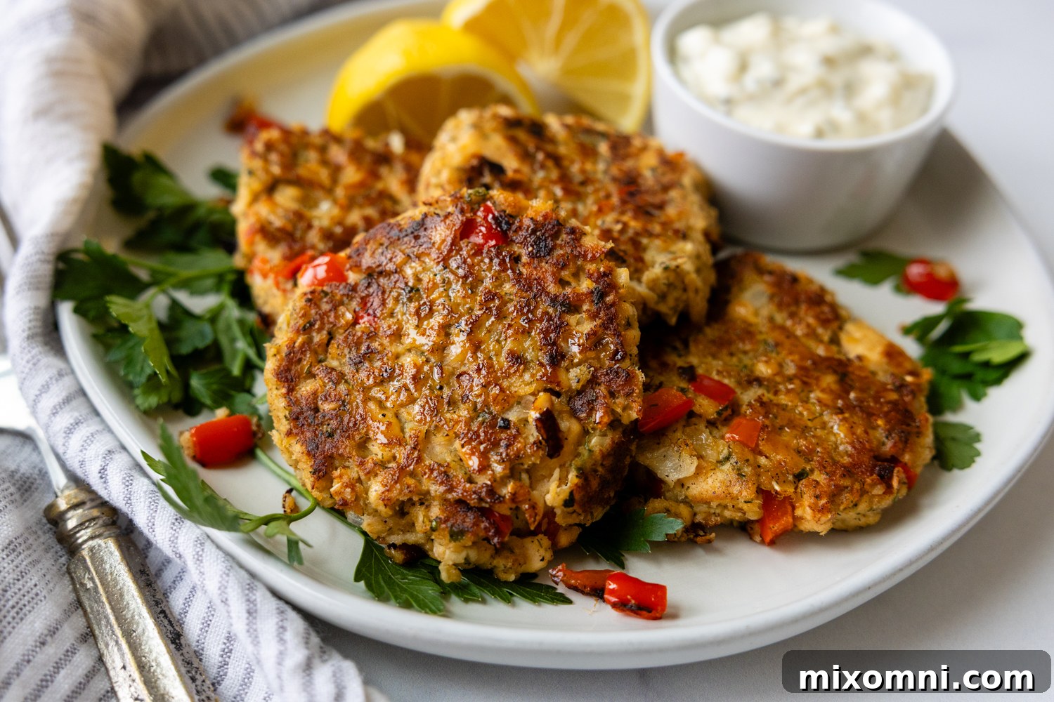 Overhead shot of salmon patties on a white plate with lemon garnish and a bowl of dipping sauce.