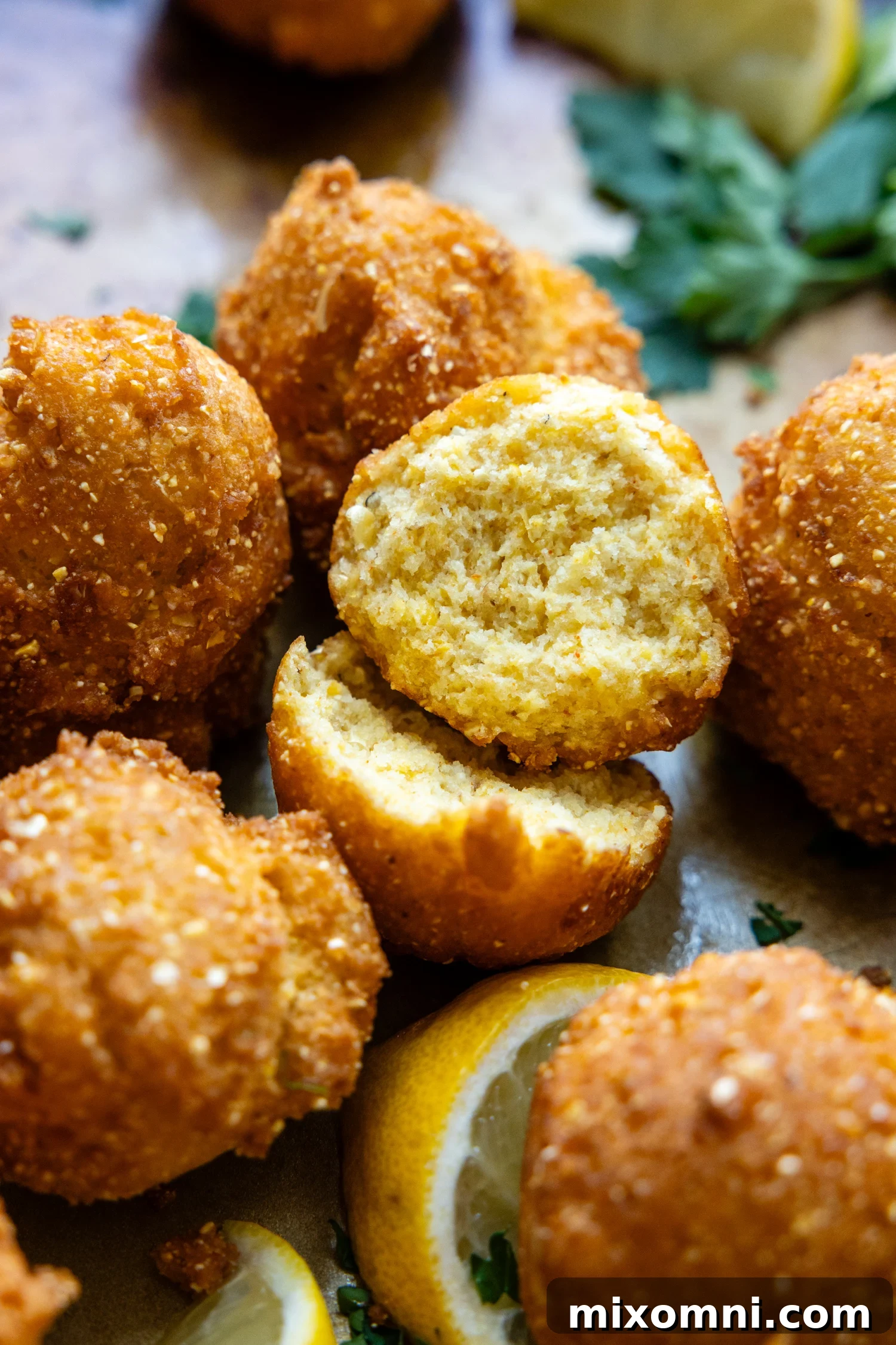 Cooked hush puppies with one cut in half showing inside texture.