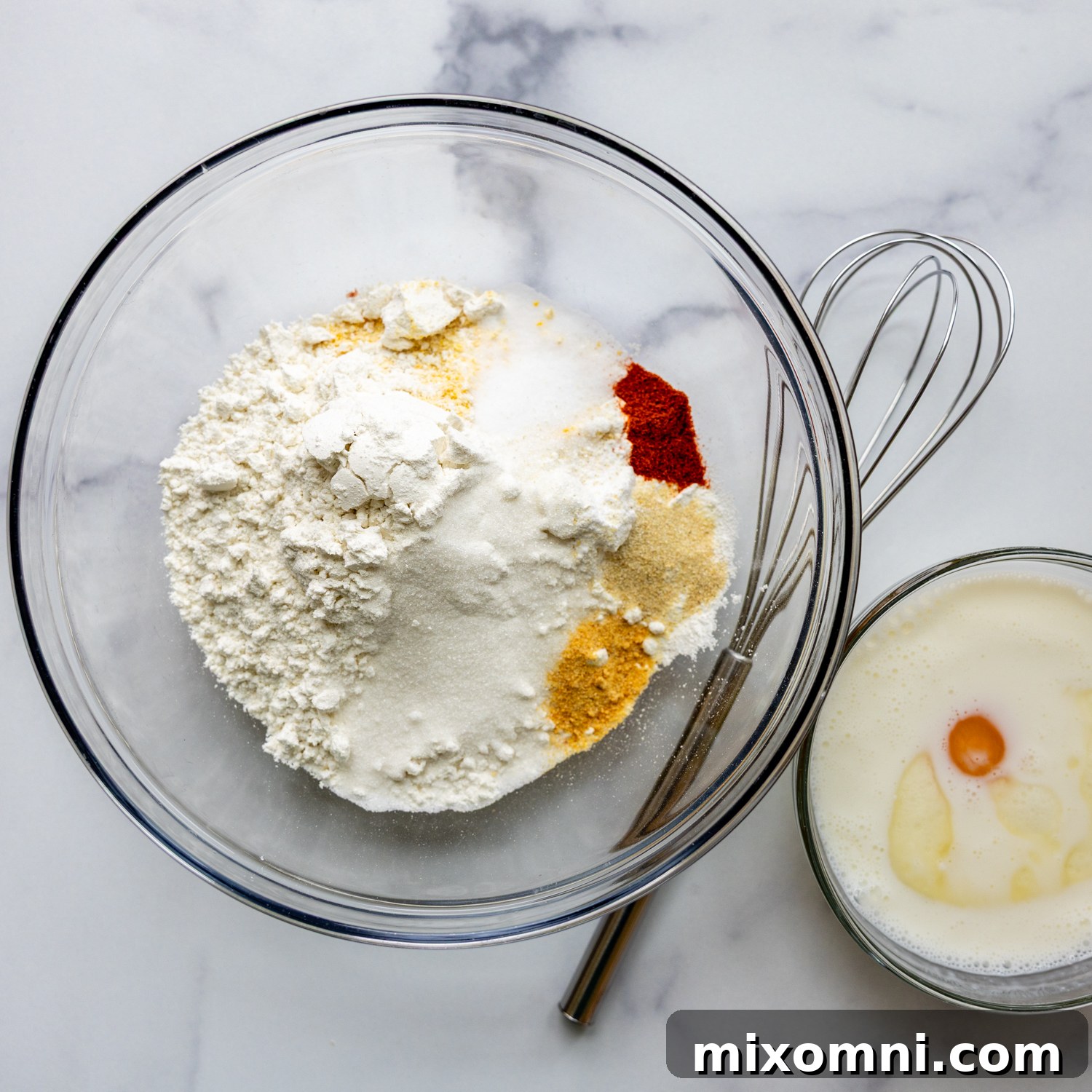 Glass bowl full of ingredients with a whisk.
