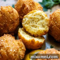 Cooked hush puppies with one cut in half showing inside texture.