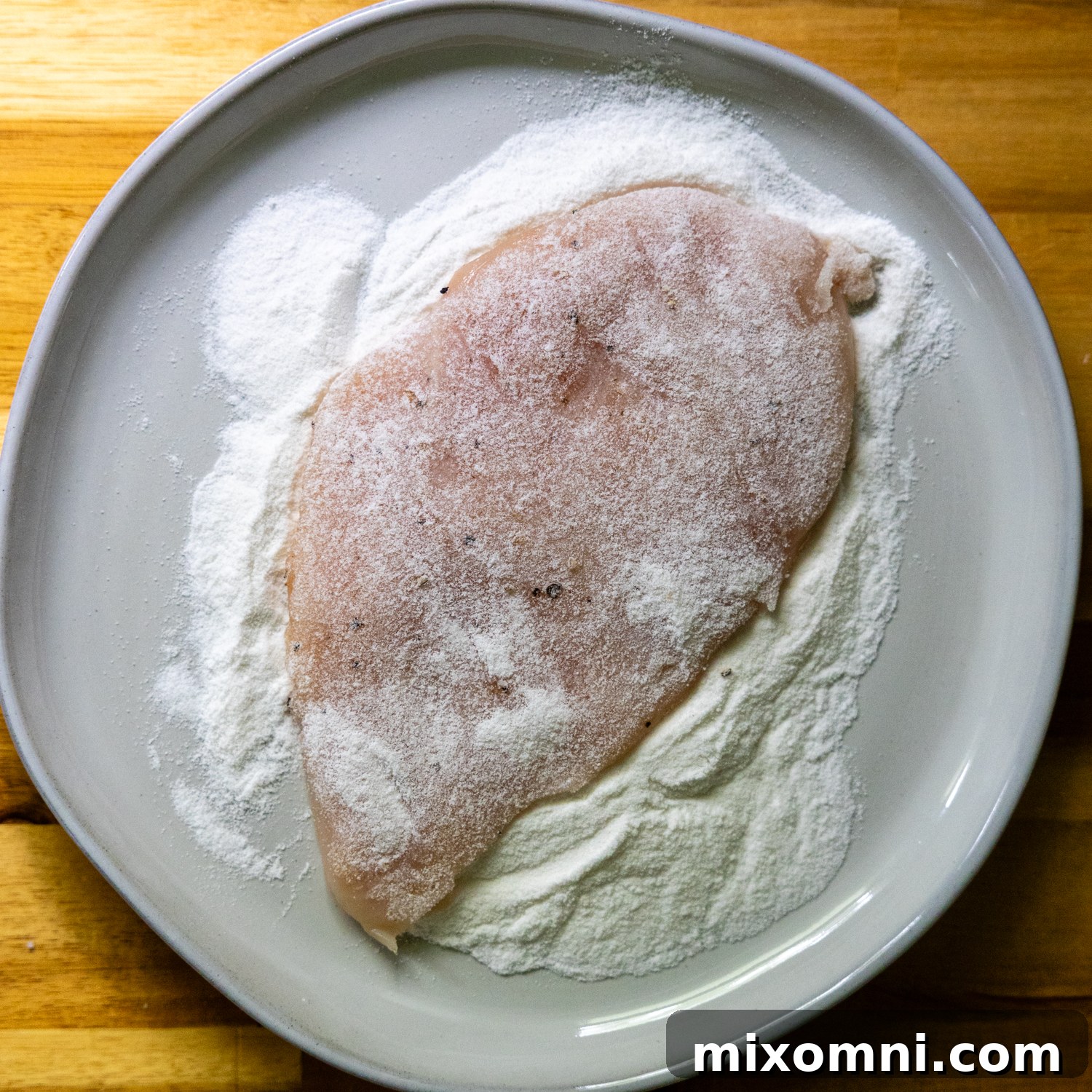 Chicken cutlet being dredged in rice flour.