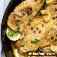 Gluten Free Chicken Piccata in a skillet with lemon garnish and topped with capers.