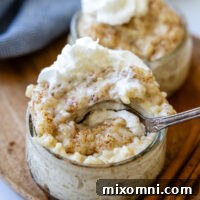 a spoon going into a small glass bowl of rice pudding with whipped cream on top.